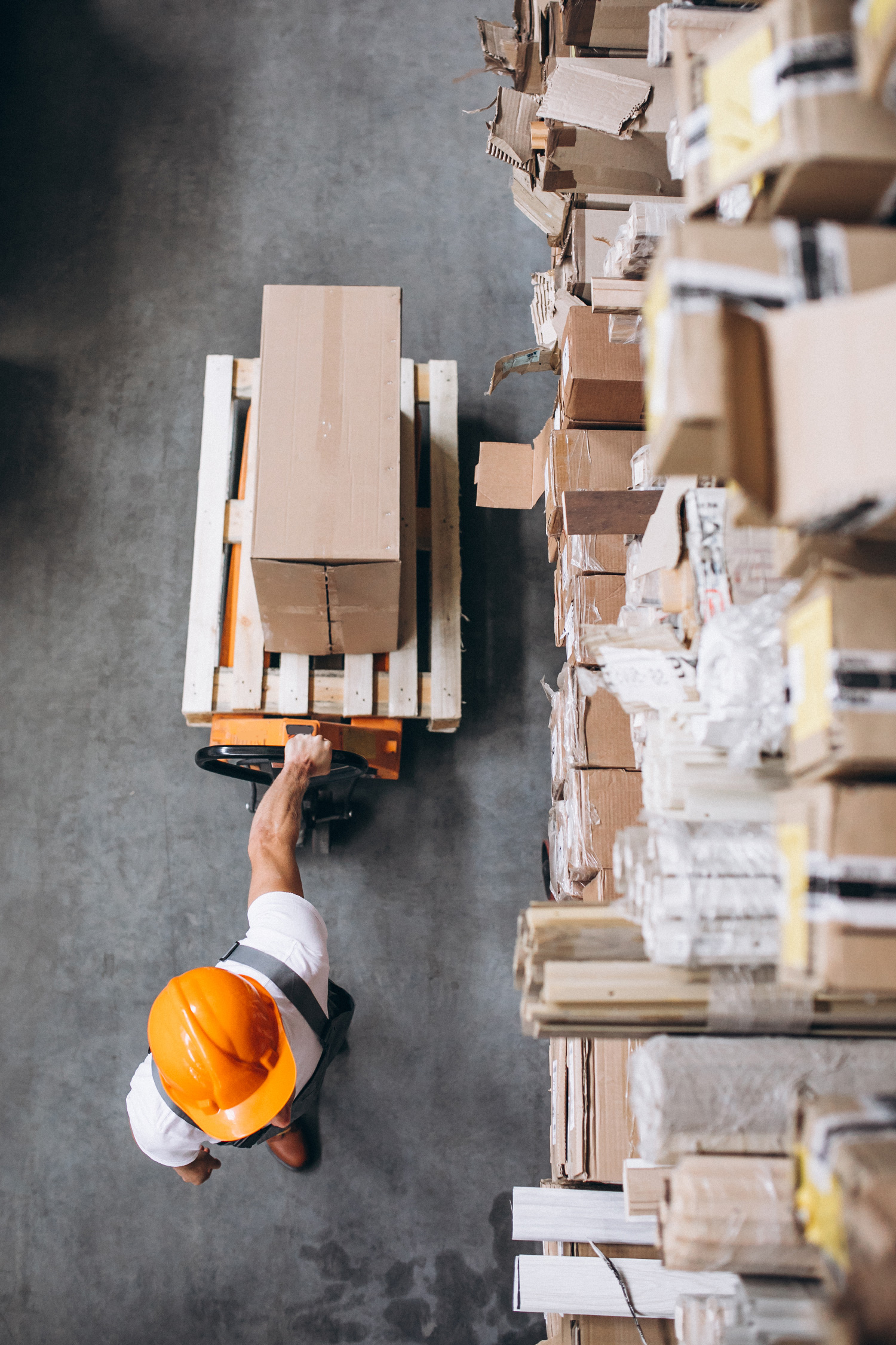 A warehouse worker moving stock on a pallet truck, seen from above